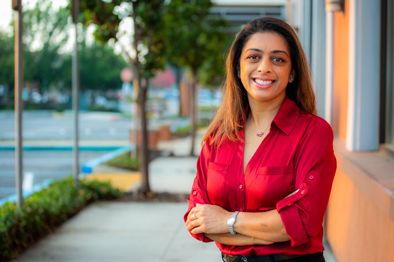 Dr. Rayani standing at the front entrance smiling with arms folded